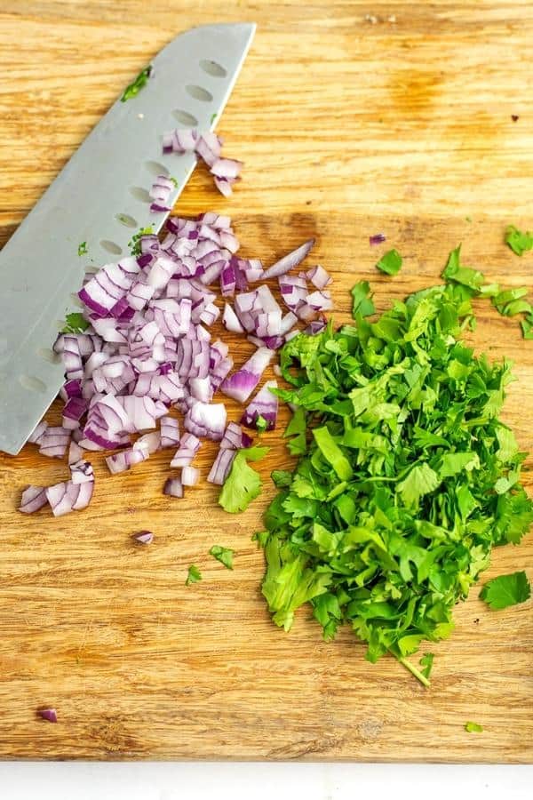 Chopped red onion and cilantro on a wood cutting board.
