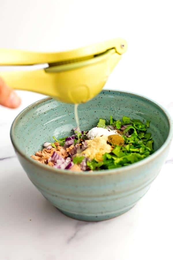 Lime juice being squeezed over the Mexican tuna salad ingredients in a blue bowl.