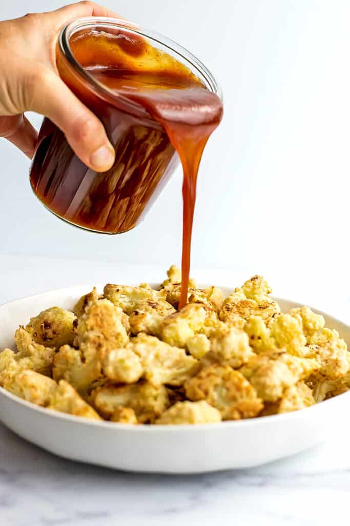 Vegan sweet and sour sauce being poured over breaded cauliflower.