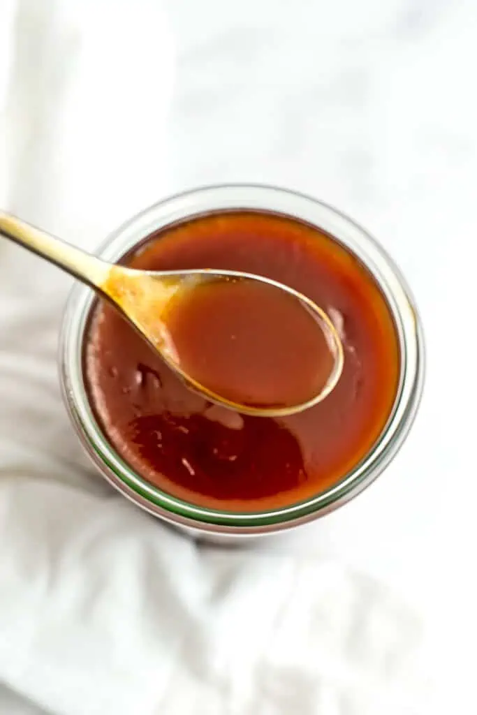Large spoonful of sweet and sour sauce over a glass jar of sauce.