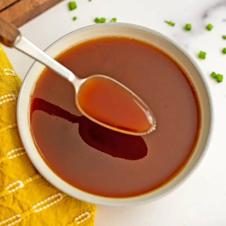 Spoonful of healthy sweet and sour sauce over a white bowl with yellow napkin.
