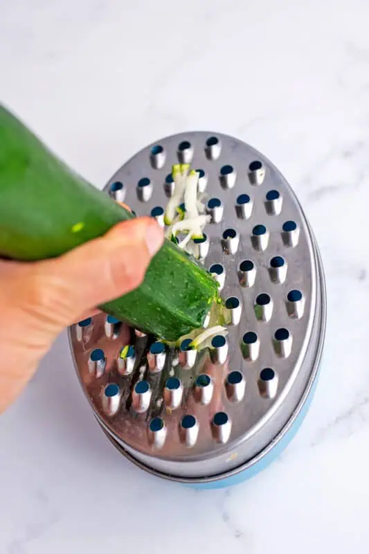 Hand holding zucchini while grating it on a grater.