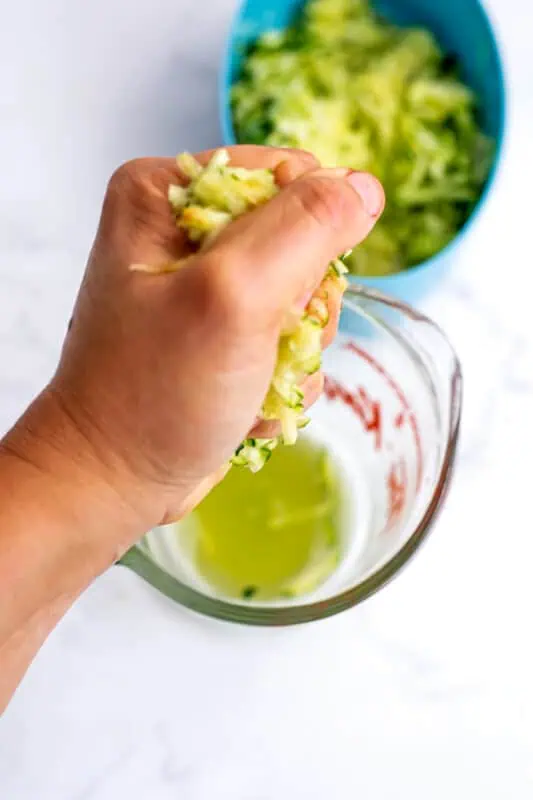 Hand squeezing out the liquid from shredded zucchini.