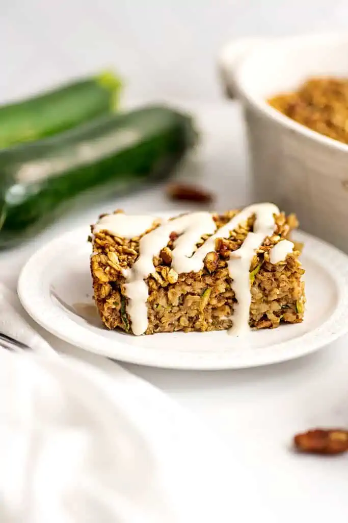 Slice of zucchini bread baked oatmeal on a white plate, drizzled with maple yogurt frosting..