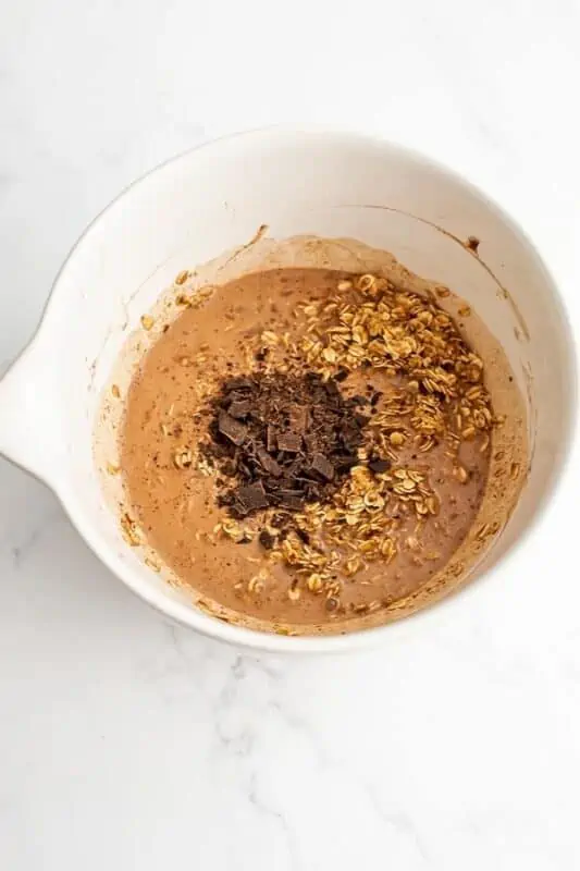 Chocolate chunks added to bowl with chocolate baked oatmeal ingredients.