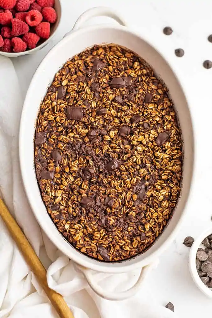 Baked chocolate oatmeal in a white casserole dish, wooden spoon on the side.