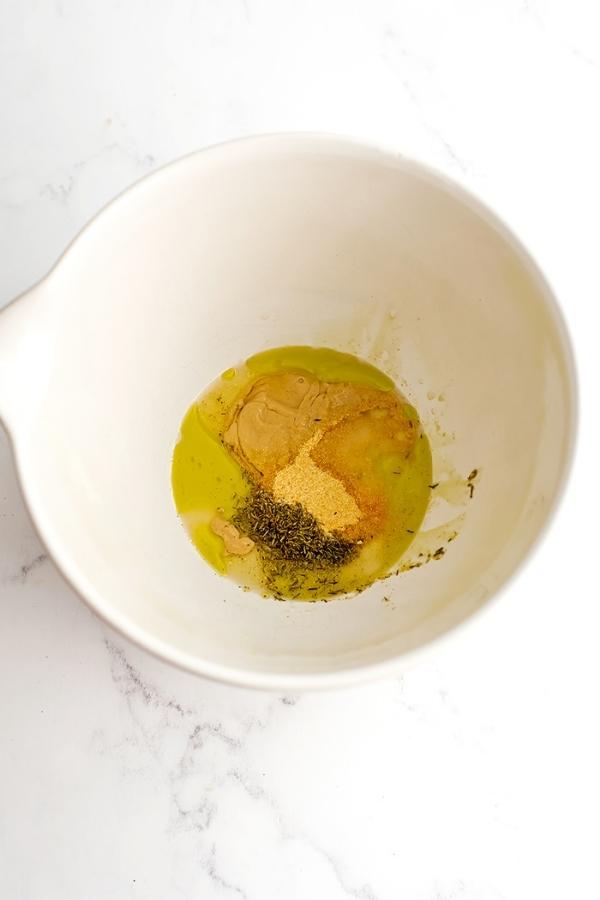 Dijon mustard, spices and olive oil in a large white bowl.