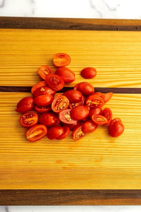 Grape tomatoes sliced in half on a cutting board.