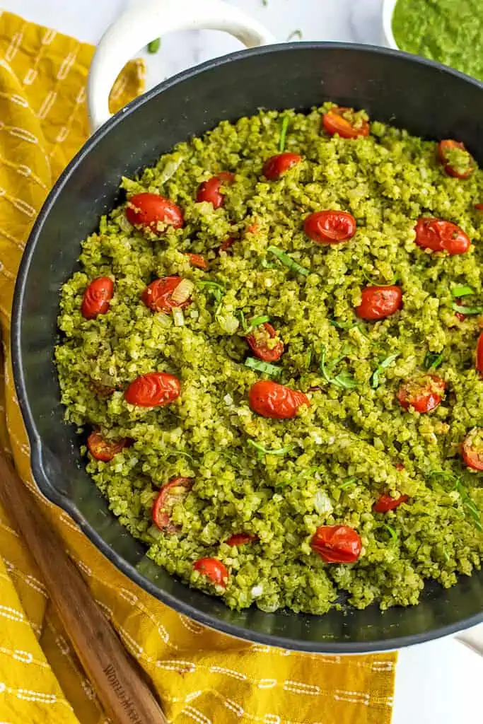 Large cast iron skillet filled with pesto cauliflower rice, with a yellow napkin on the side.