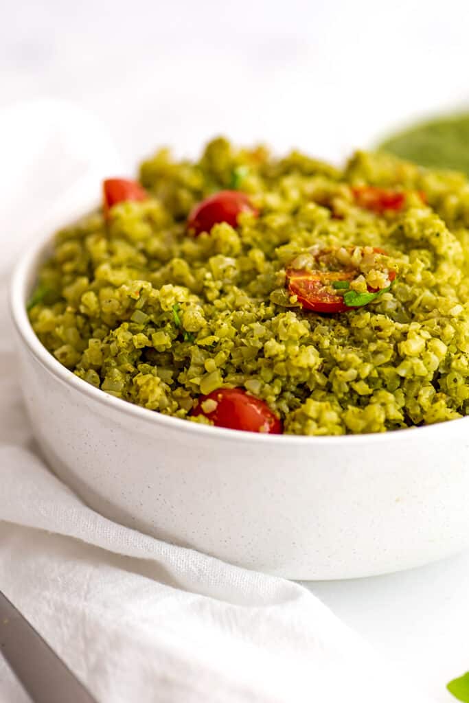 White bowl filled with pesto cauliflower rice with a white napkin on the side.