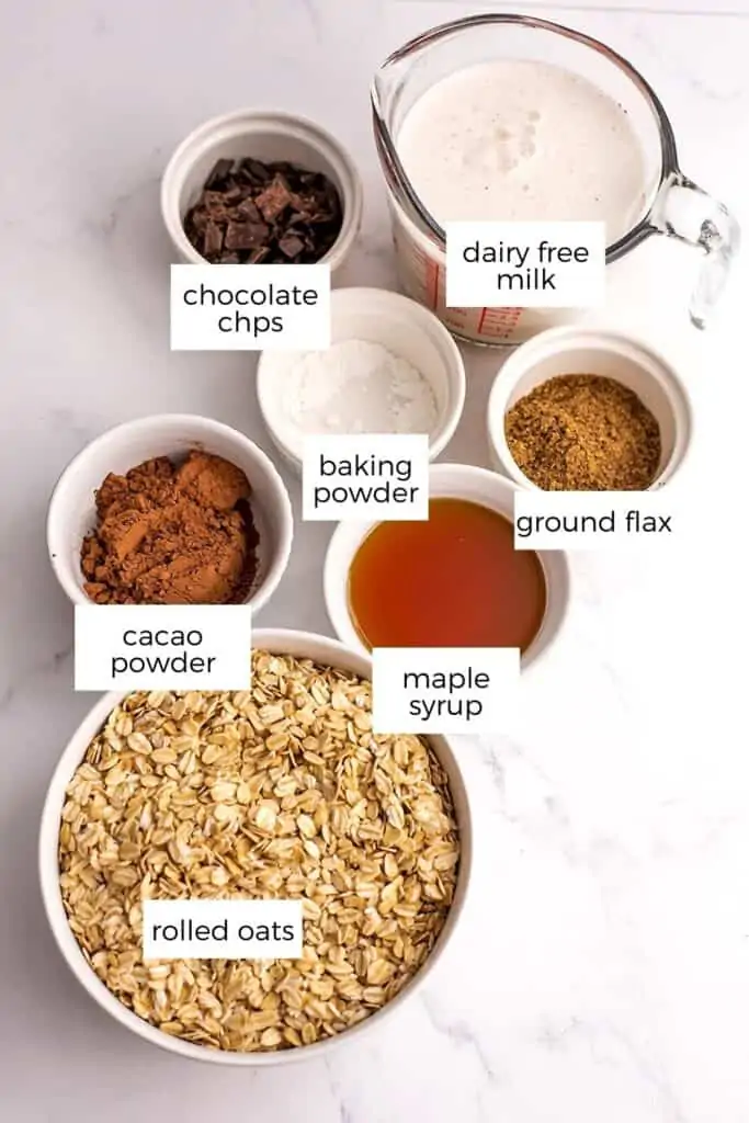 Chocolate baked oatmeal ingredients in white bowls on a marble countertop.