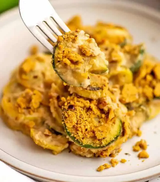 Fork holding cracker coated zucchini as part of healthy squash casserole dish.