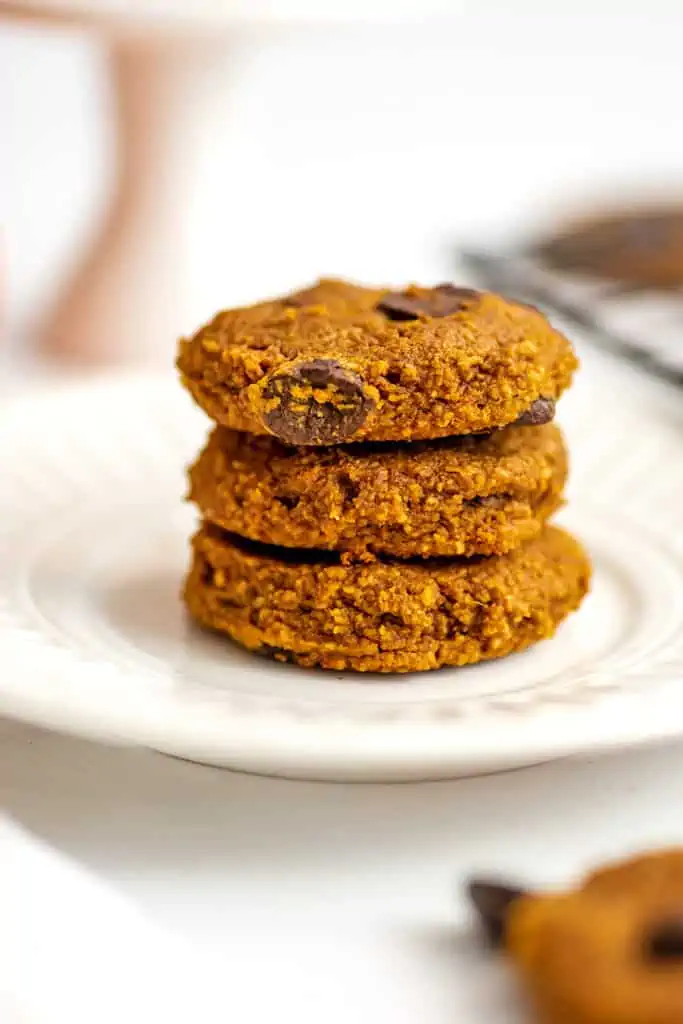 White plate with three pumpkin gluten free chocolate chip cookies stacked on top.
