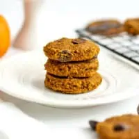 Three almond flour pumpkin cookies stacked on a white plate.