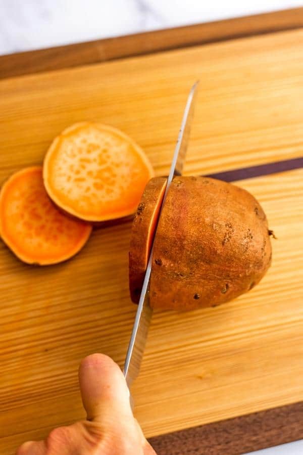 Knife cutting sweet potato into 1/2 inch slices.