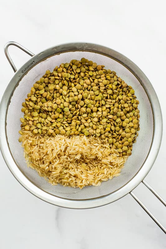 Mesh strainer filled with brown lentils and brown rice. 