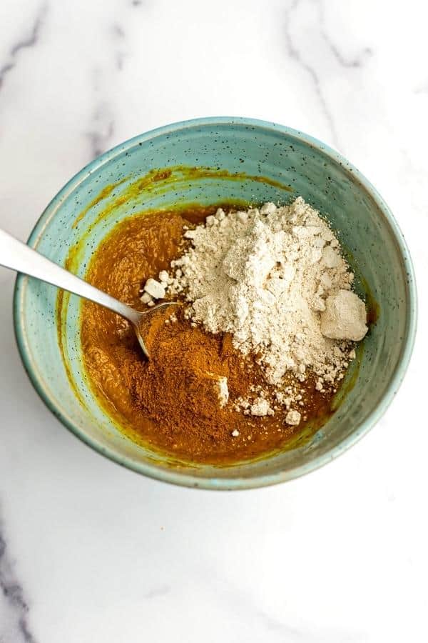 Flour and spices added to pumpkin mixture in green bowl.