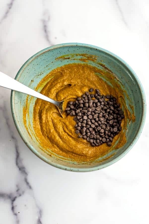 Mini chocolate chips added to pumpkin batter in green bowl.