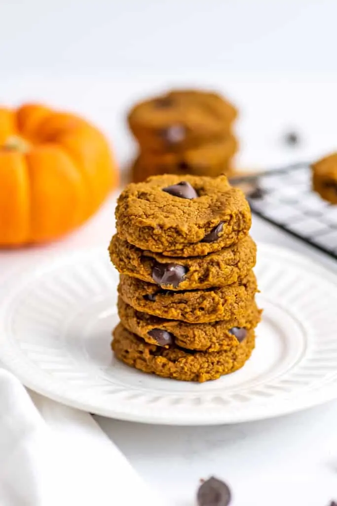 Five oat flour pumpkin cookies stacked on a white plate.