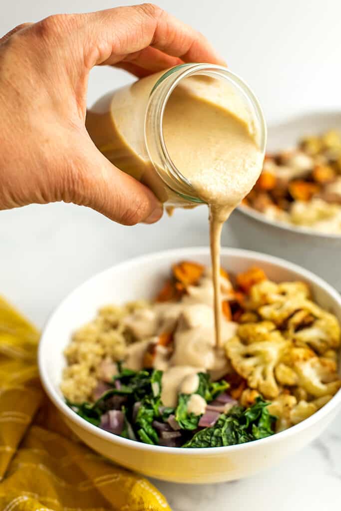 Maple tahini dressing being poured over a quinoa bowl.
