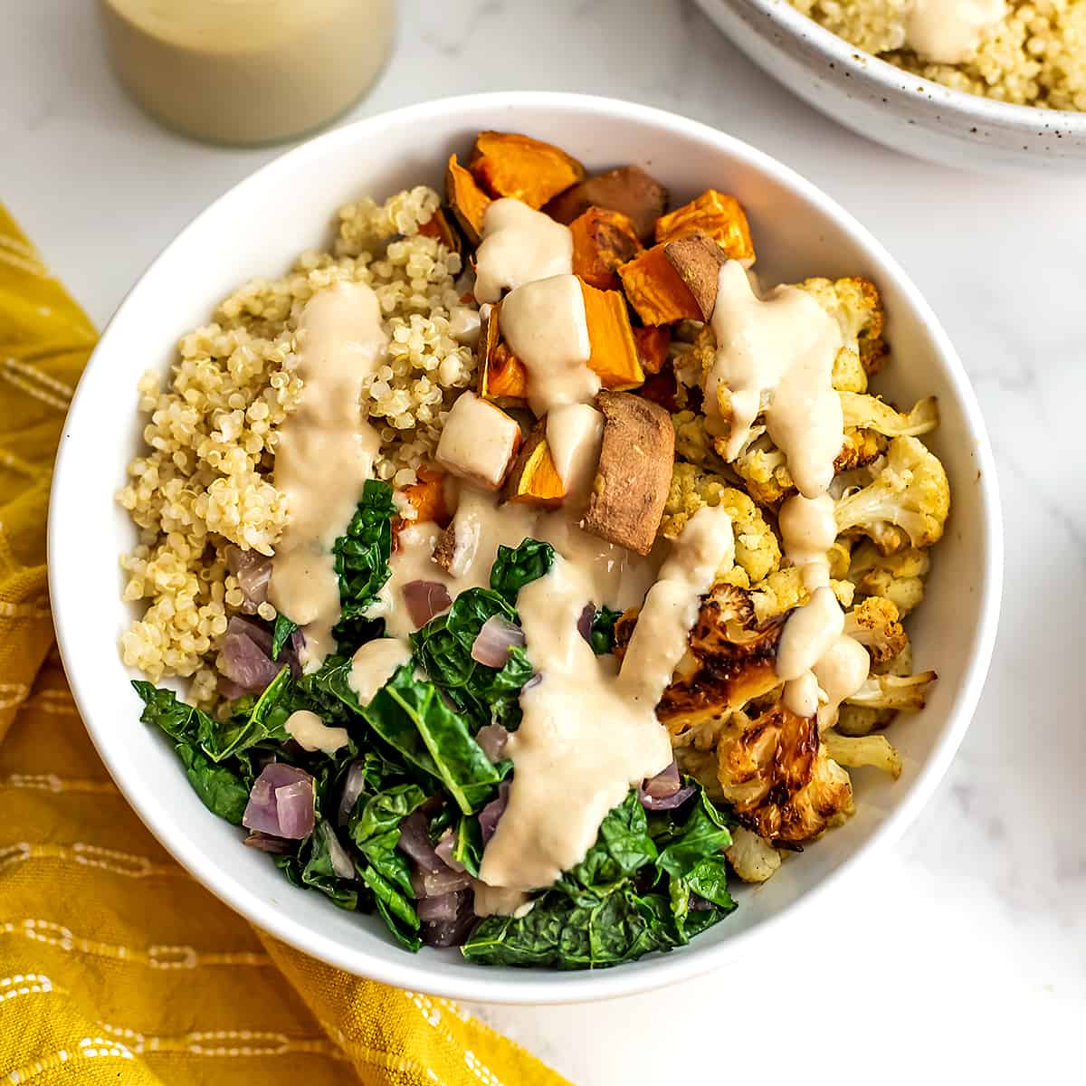 Kale sweet potato quinoa bowl with maple tahini dressing drizzled over top.