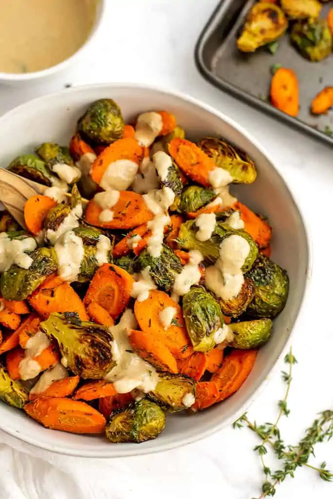 Large white bowl filled with roasted brussel sprouts with carrots with tahini drizzle.