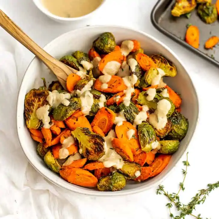 Tahini drizzle on top of bowl filled with roasted brussel sprouts and carrots.