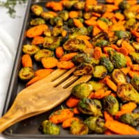 Wooden spatula on a baking sheet with roasted brussel sprouts and carrots.