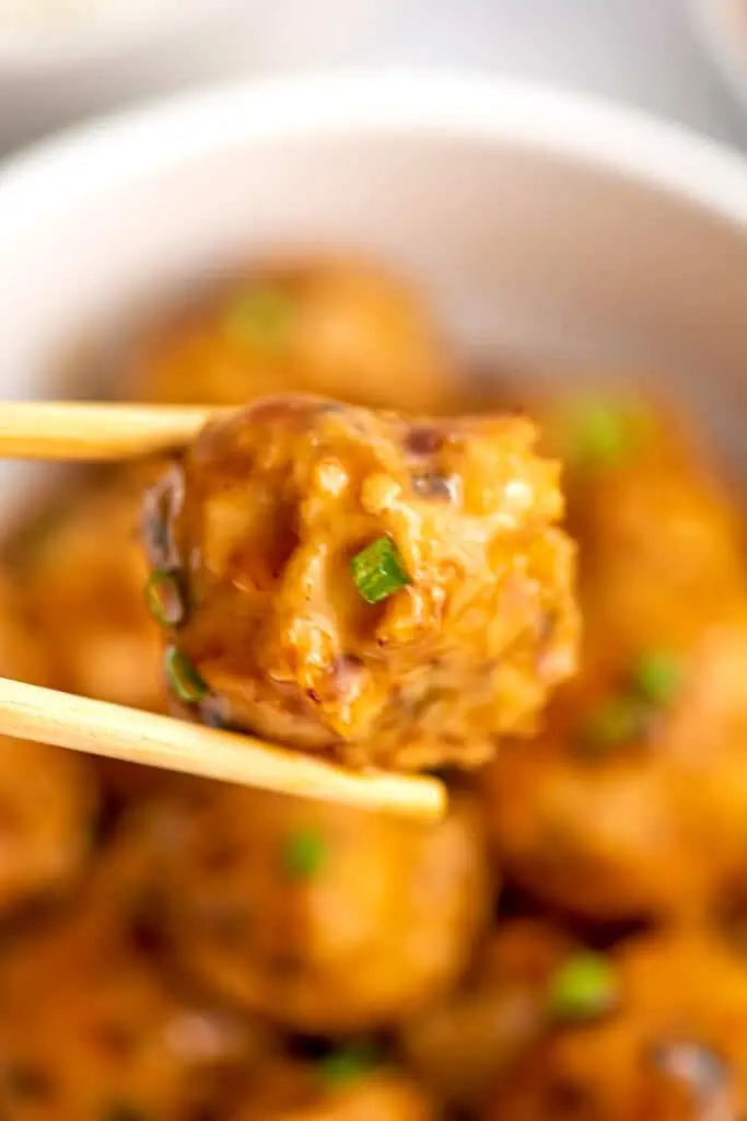 Sweet and sour chicken meatballs being picked up by wooden chopsticks.