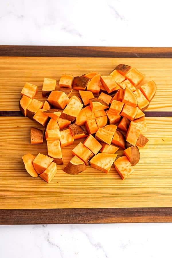 Sweet potato cut into cubes on a wooden cutting board.