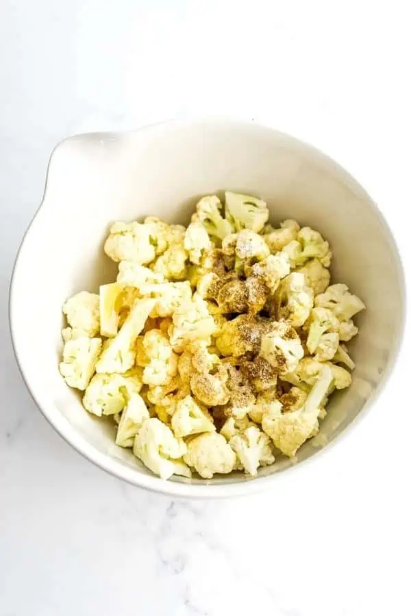Cauliflower florets in a white bowl with spices on top.