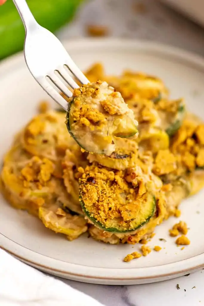 Fork holding cracker coated zucchini as part of healthy squash casserole dish.