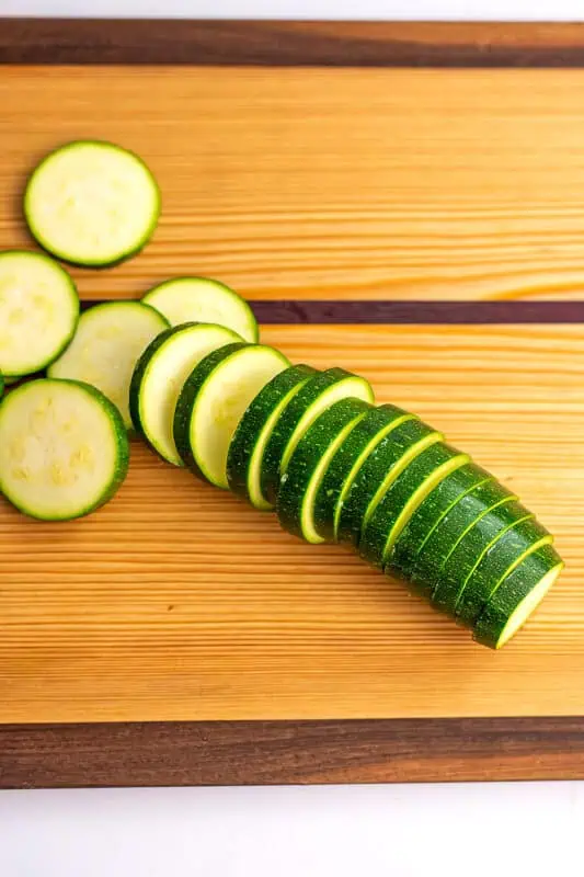 Zucchini cut into 1/2 inch coins on a wood cutting board.