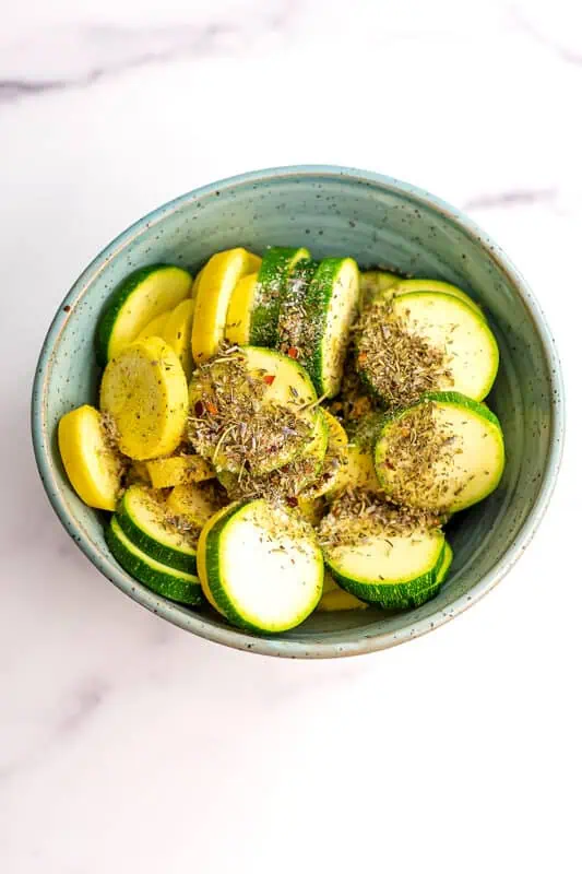 zucchini and yellow squash in a bowl with spices before air frying.