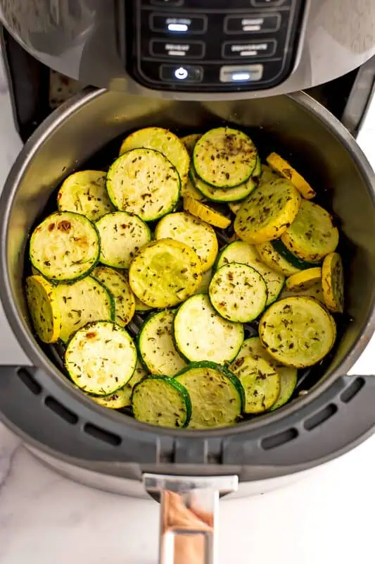 Zucchini and yellow squash in air fryer basket before shaking the basket.