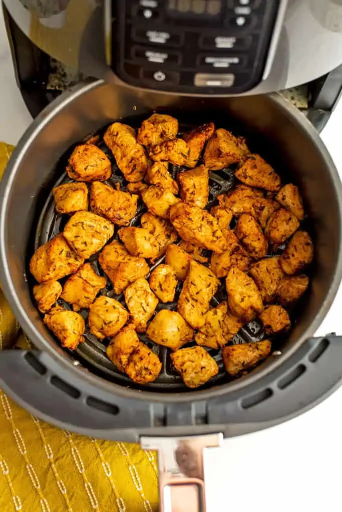 Chicken cubes in air fryer basket after cooking. Yellow napkin on the side.