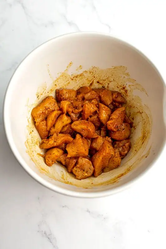Diced chicken covered in spices in a large white bowl
