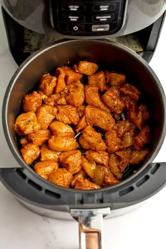 Raw chicken bites in air fryer basket before cooking.
