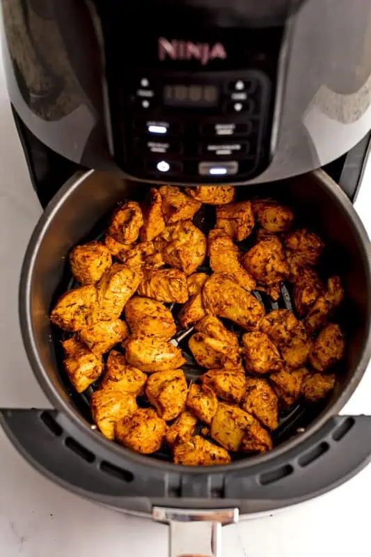 Chicken cubes in air fryer basket after turning.