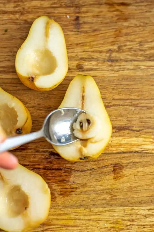 Spoon removing the seeds from pear halves.