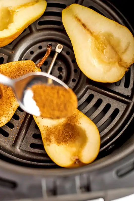 Spoon sprinkling the cinnamon sugar mixture over pears in air fryer.