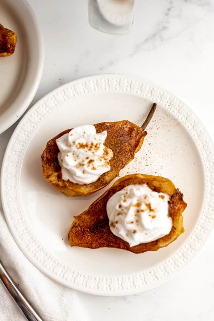 Air fryer pears on white plate with whipped cream on top.