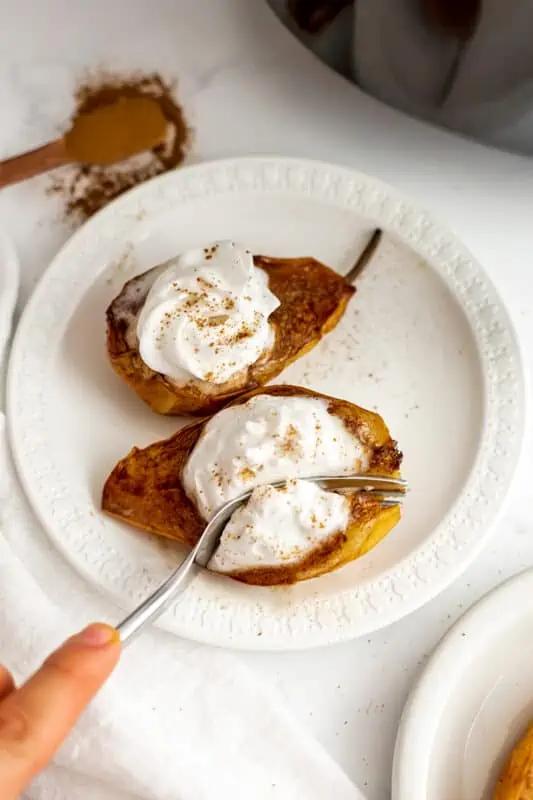 Fork cutting into an air fried pear with whipped cream.