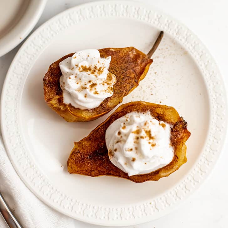 Air fryer pears with whipped cream on top on a white plate.