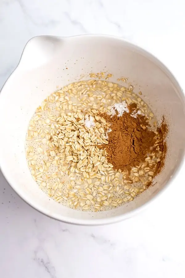 Oats, cinnamon and baking powder added to white bowl.