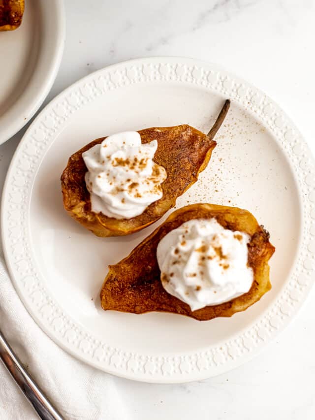 Air fryer pears on white plate with whipped cream on top.