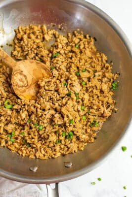 Ground chicken stir fry in stainless skillet with wooden spoon.