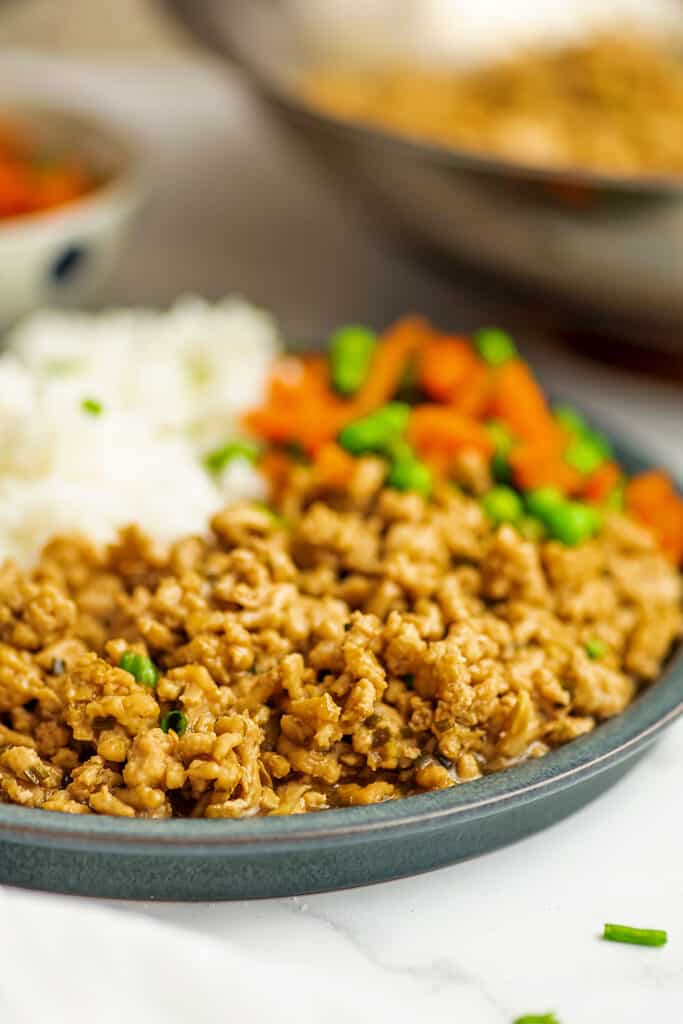 Ground chicken stir fry on a grey plate with rice, peas and carrots.