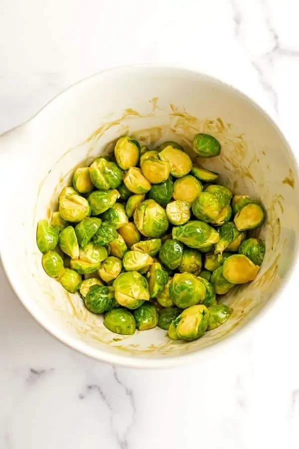 Maple mustard sauce over sliced brussel sprouts in white bowl.