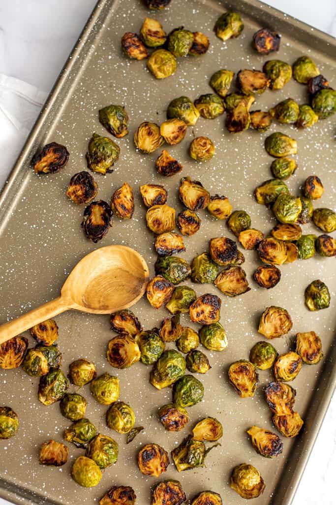 Baking sheet filled with maple dijon brussel sprouts with wooden spoon.